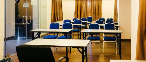 Un salón de conferencias con mesas, sillas, un muro de cristal y cortinas.