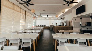 A modern dining area with white tables and chairs, ceiling fans, and a kitchen counter in the background. - Kertih Damansara Inn (Kerteh)