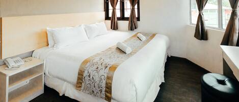 Una cama bien hecha con sábanas blancas, una mesita de noche con un teléfono y una ventana con cortinas.