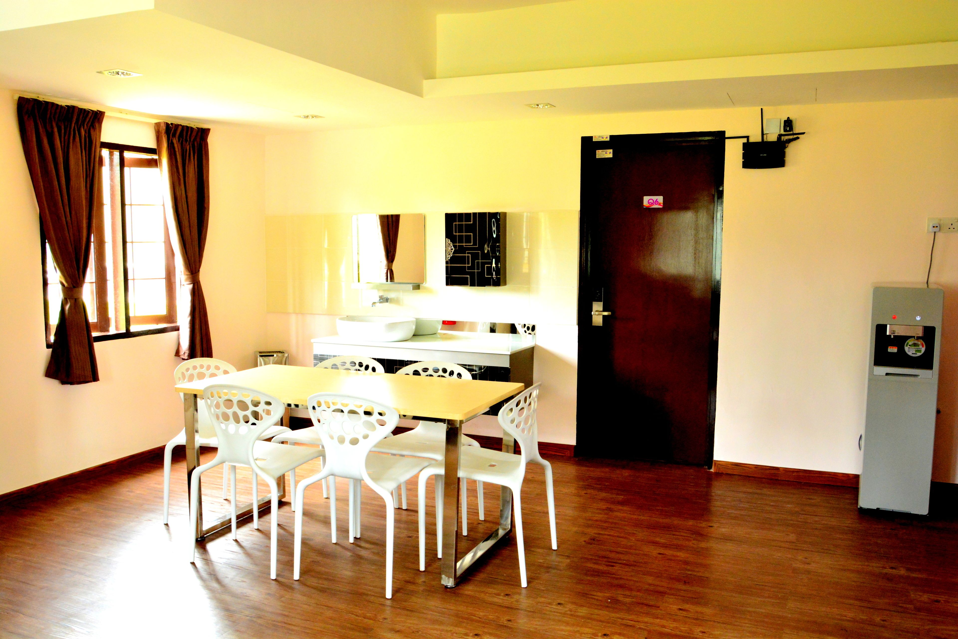 A dining area with a wooden table and white chairs, a kitchen area with cabinets and a refrigerator, and a door with a sign.