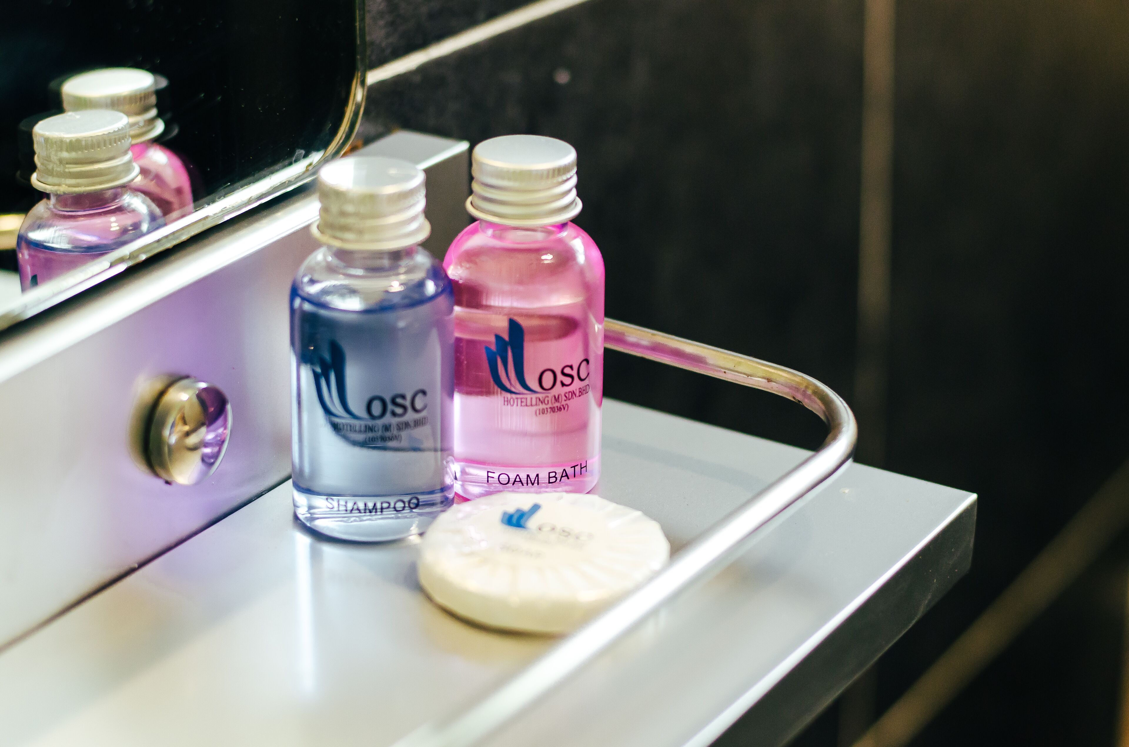 A bathroom counter with two bottles of shampoo and a bottle of foam bath.