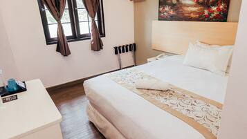 Quarto de hotel com cama, escrivaninha, ar condicionado, janela com cortinas e um quadro na parede.