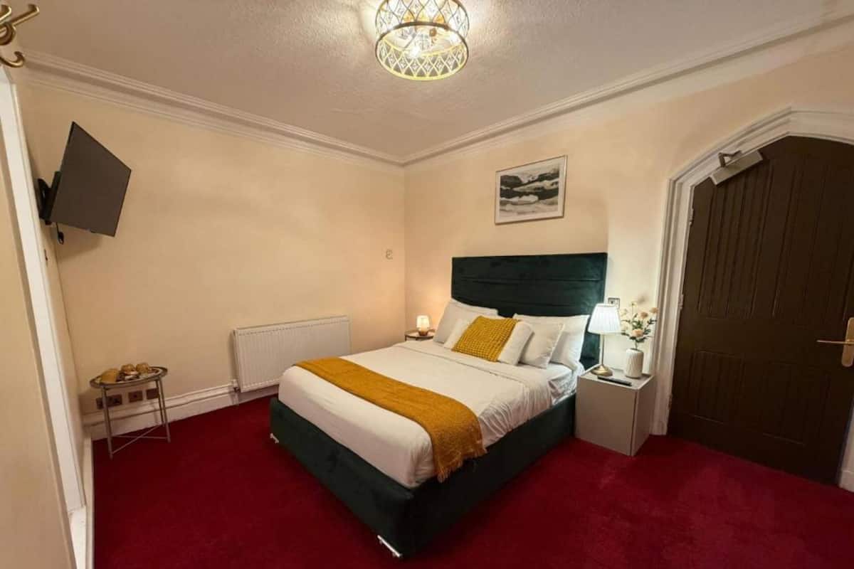 Una habitación de hotel con una cama, una mesita de noche, una lámpara, un cuadro en la pared y una puerta.