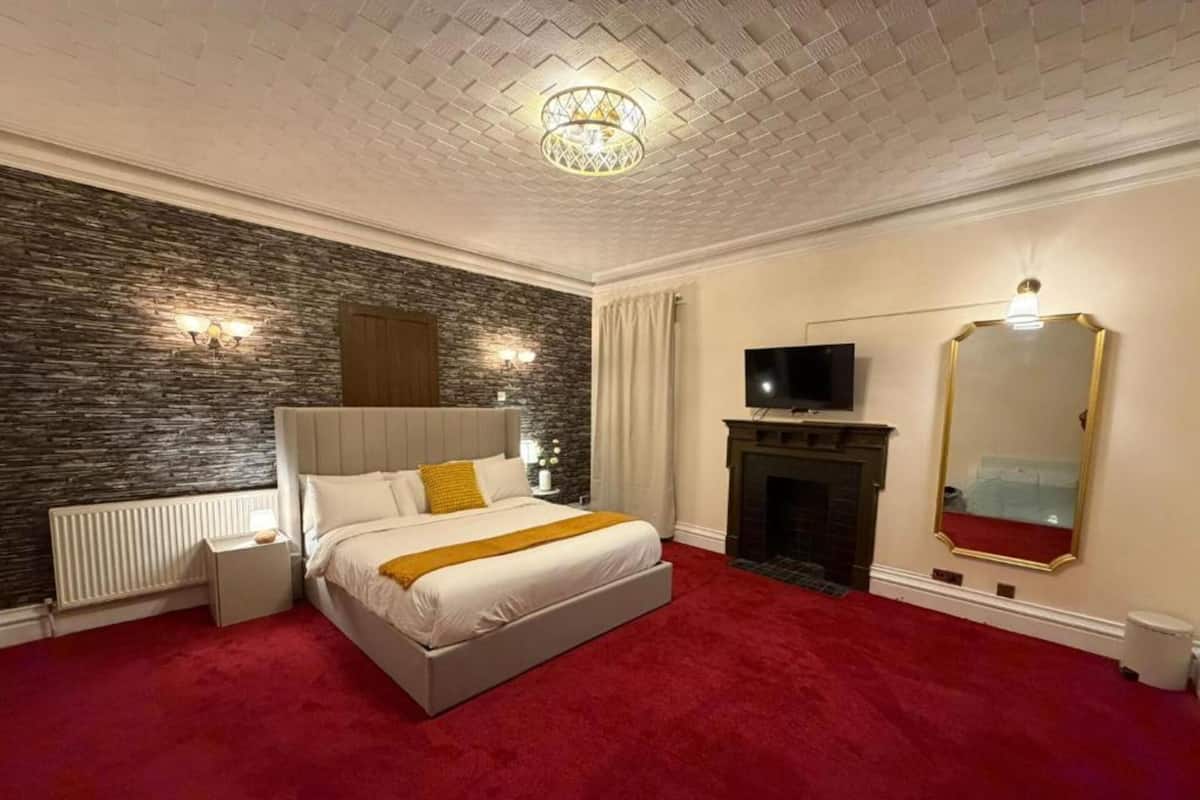 Un dormitorio con pared de piedra, chimenea, televisor y un espejo grande.