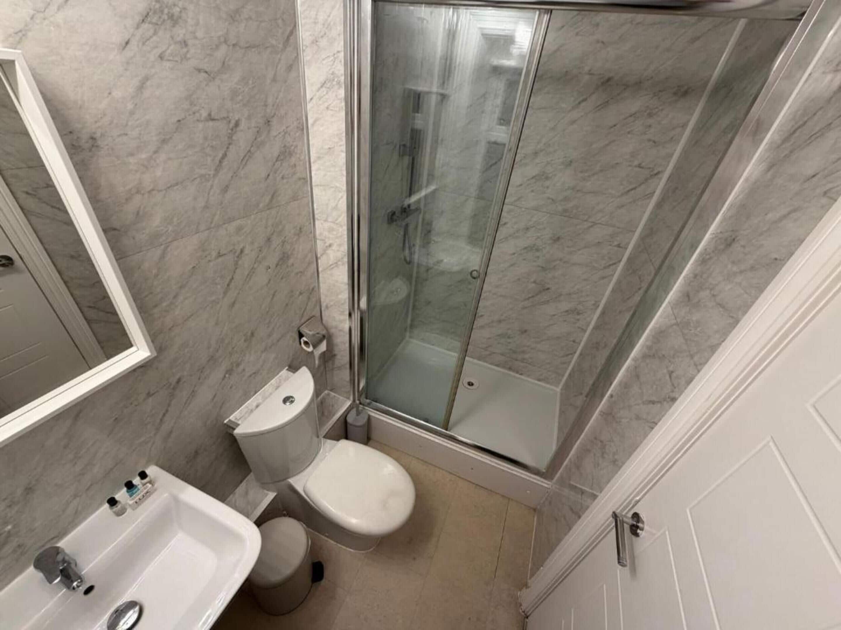 A bathroom with a toilet, sink, and glass shower enclosure.