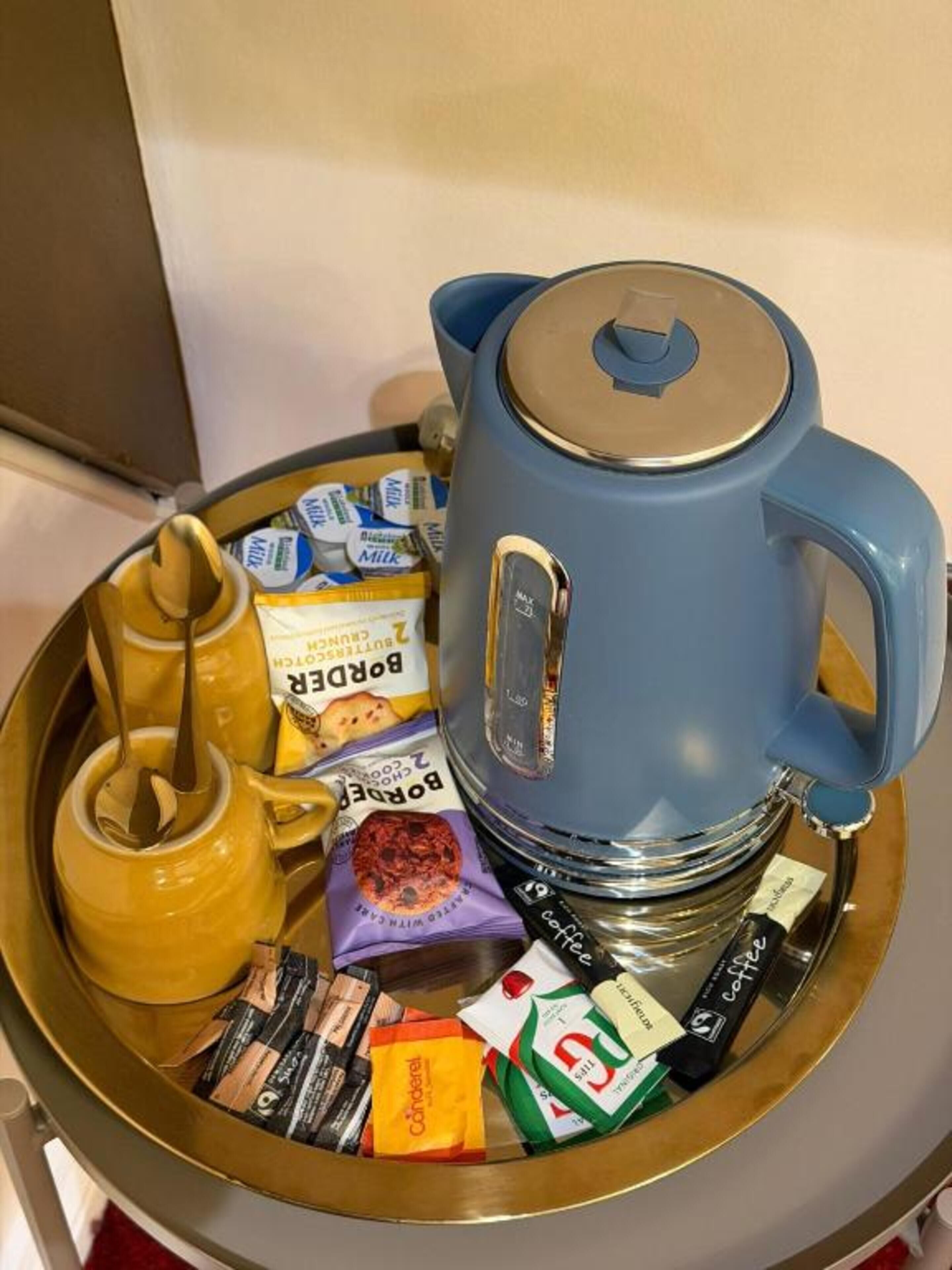 A coffee maker, a yellow teapot, and various coffee and tea packets on a tray.