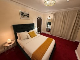 A hotel room with a bed, a nightstand, a lamp, a mirror, and a window with curtains.