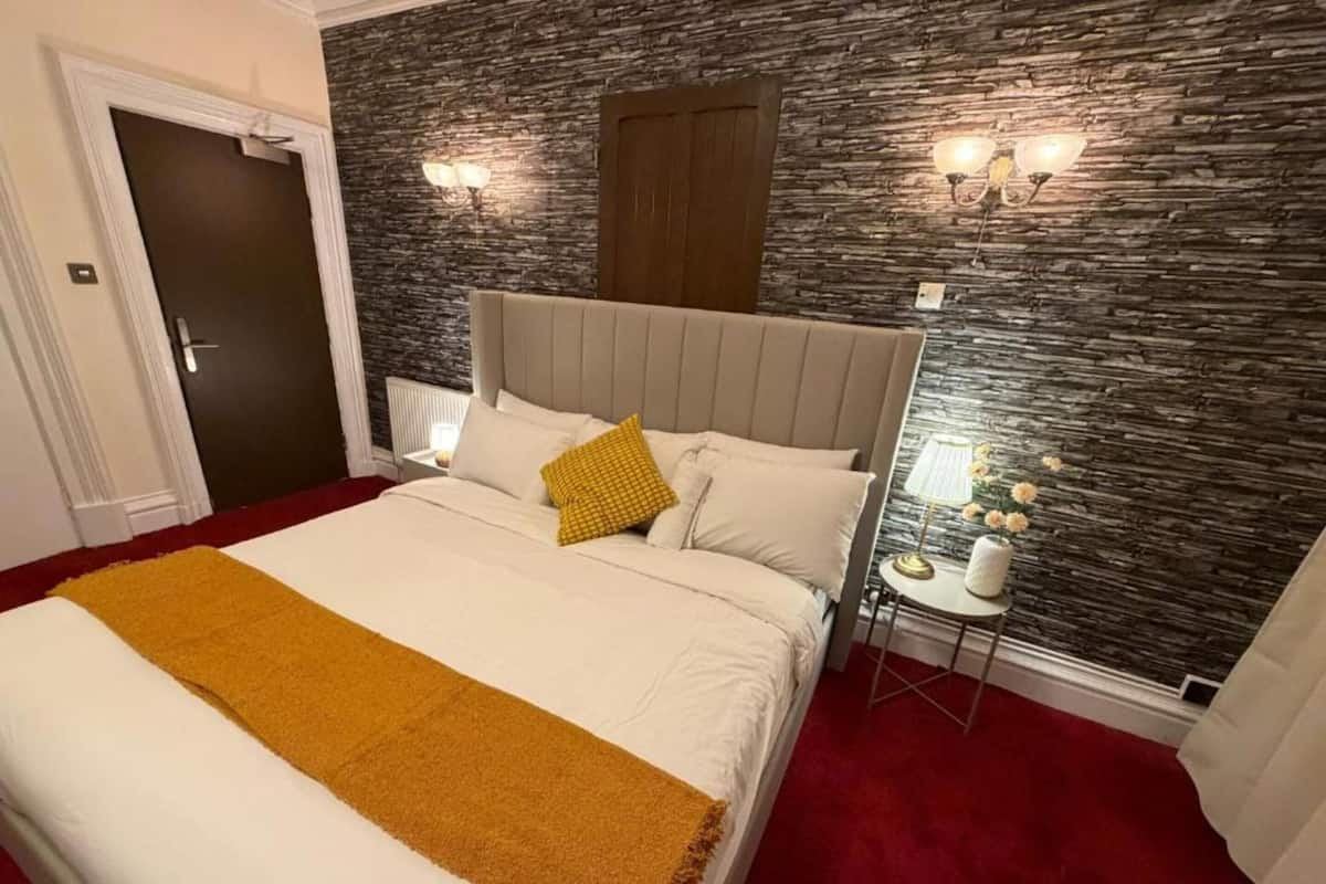 Un dormitorio con una cama grande, una pared de piedra, una puerta de madera y dos lámparas fijadas a la pared.