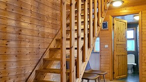 Una escalera de madera que sube a un nivel superior, una puerta de madera y vista a un baño.