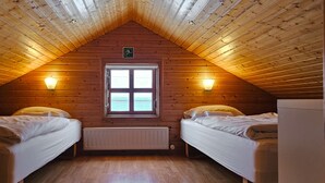 Un dormitorio acogedor en el ático, con dos camas individuales, una ventana y dos luces fijadas a la pared.
