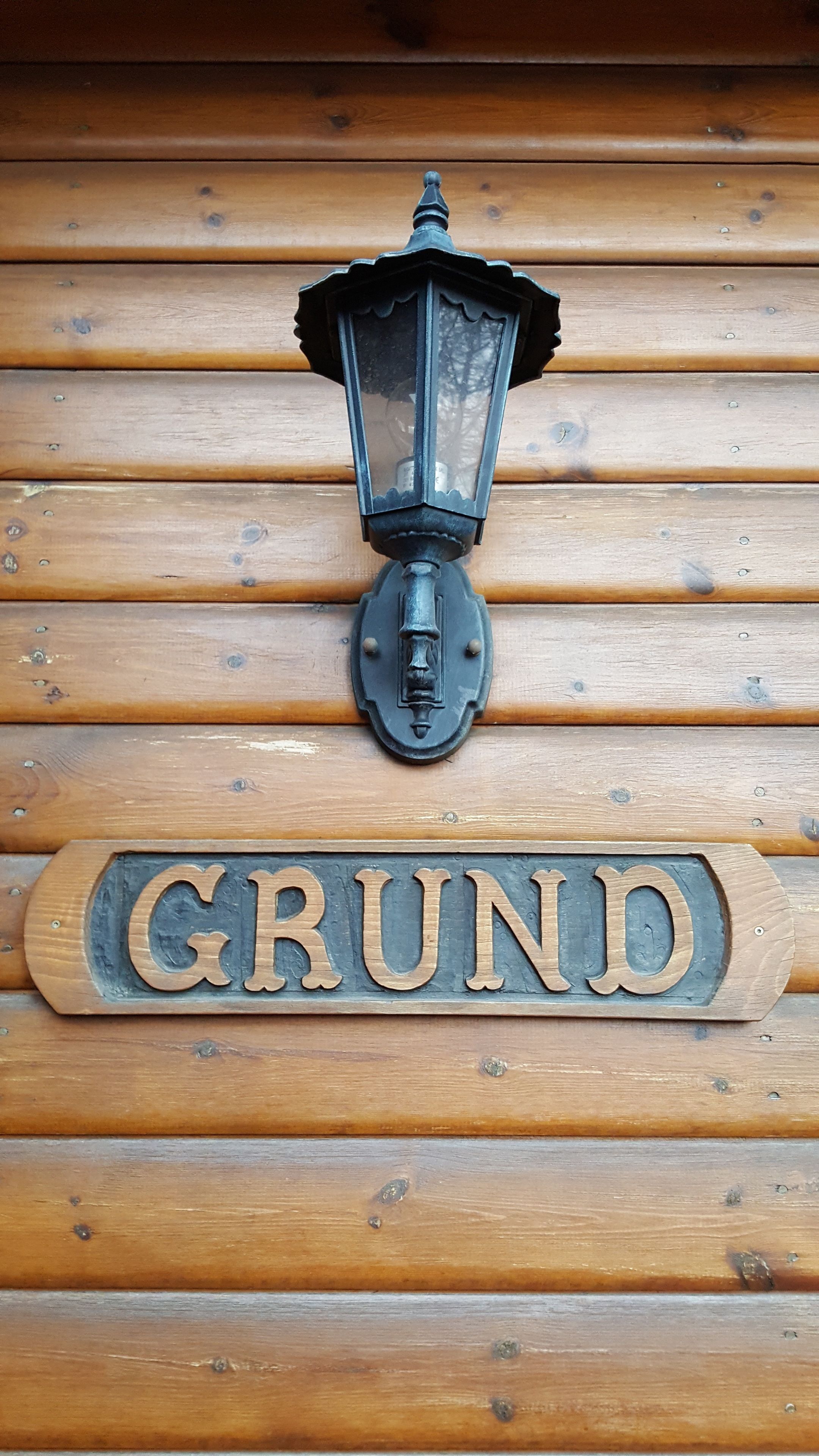 Un mur en bois, orné d’une lanterne noire et d’une enseigne sur laquelle on peut lire « GRUND ».