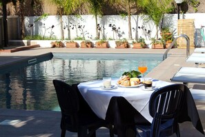 A poolside dining area with a table set for two, a glass of orange juice, and a plate of croissants.