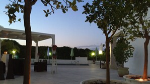 An outdoor patio area with a pergola, seating, potted plants, and a fire feature. - B&B Marricriu (Avola)