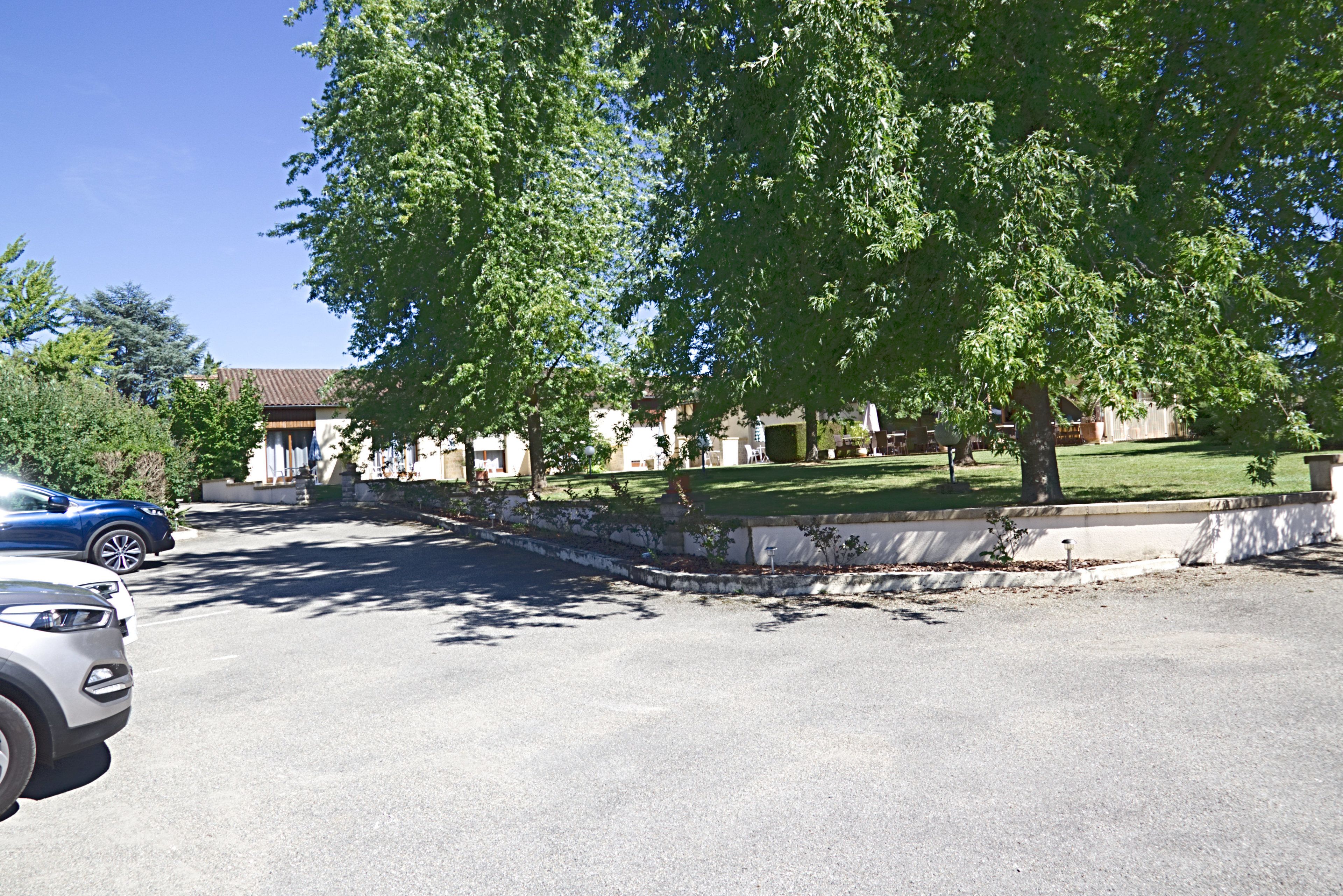 Una calle residencial con coches aparcados, un árbol grande y casas con césped cuidado.