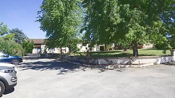 Una calle residencial con coches aparcados, un árbol grande y casas con césped cuidado.
