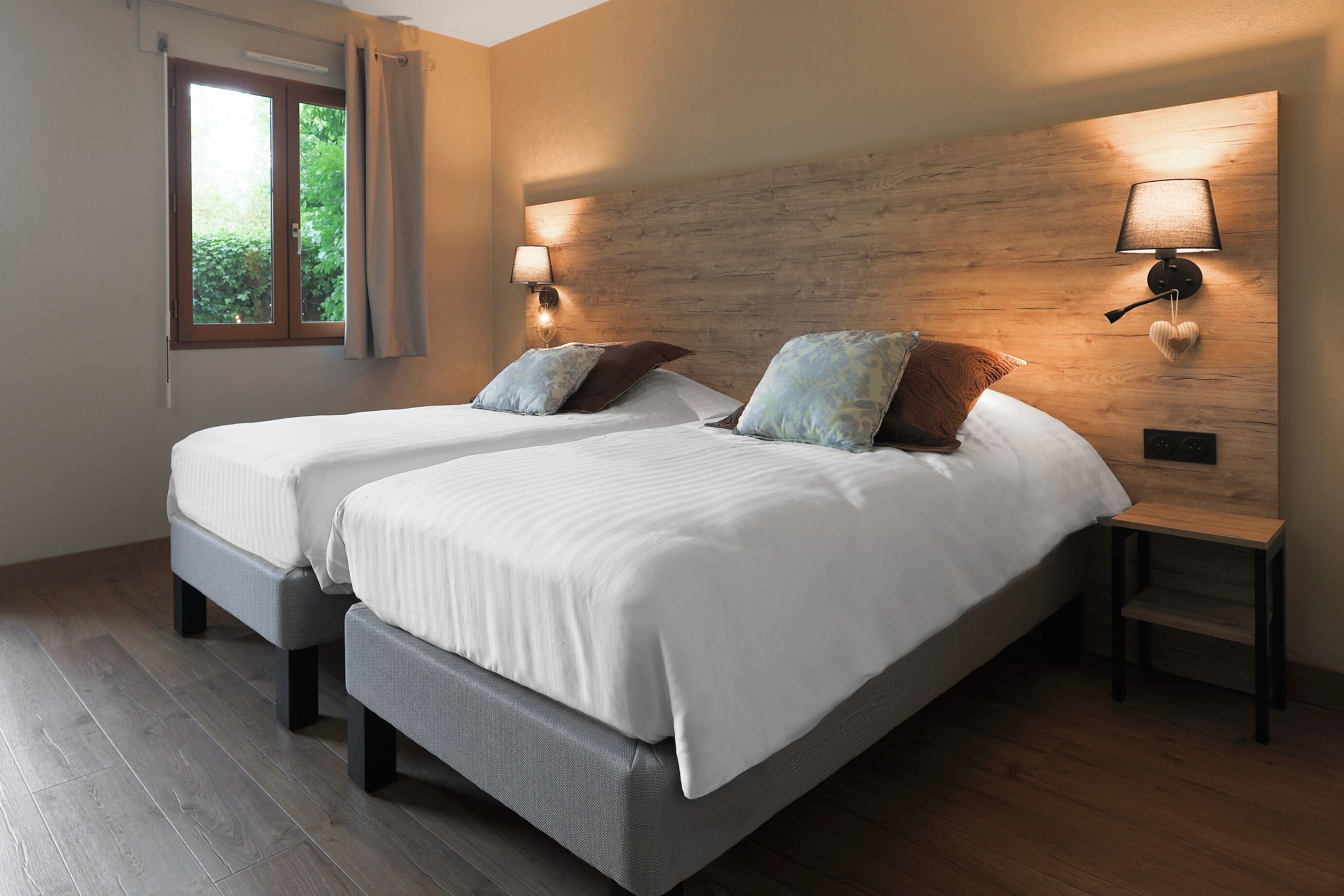 A double bed with two bedside tables, a window with curtains, and a wall-mounted lamp.