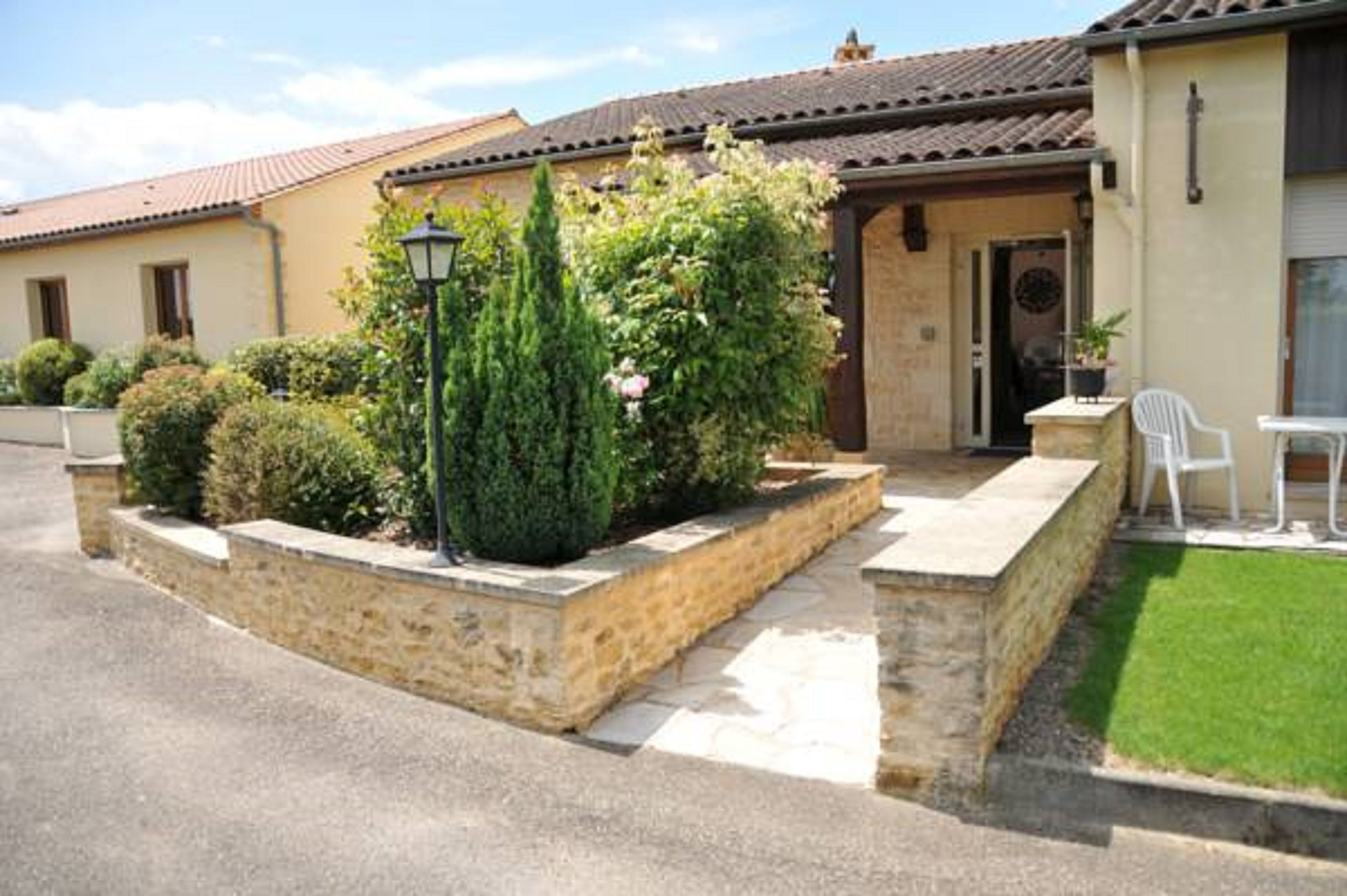 A residential building with a tiled roof, a stone entrance, and a small garden area with a lawn and potted plants.
