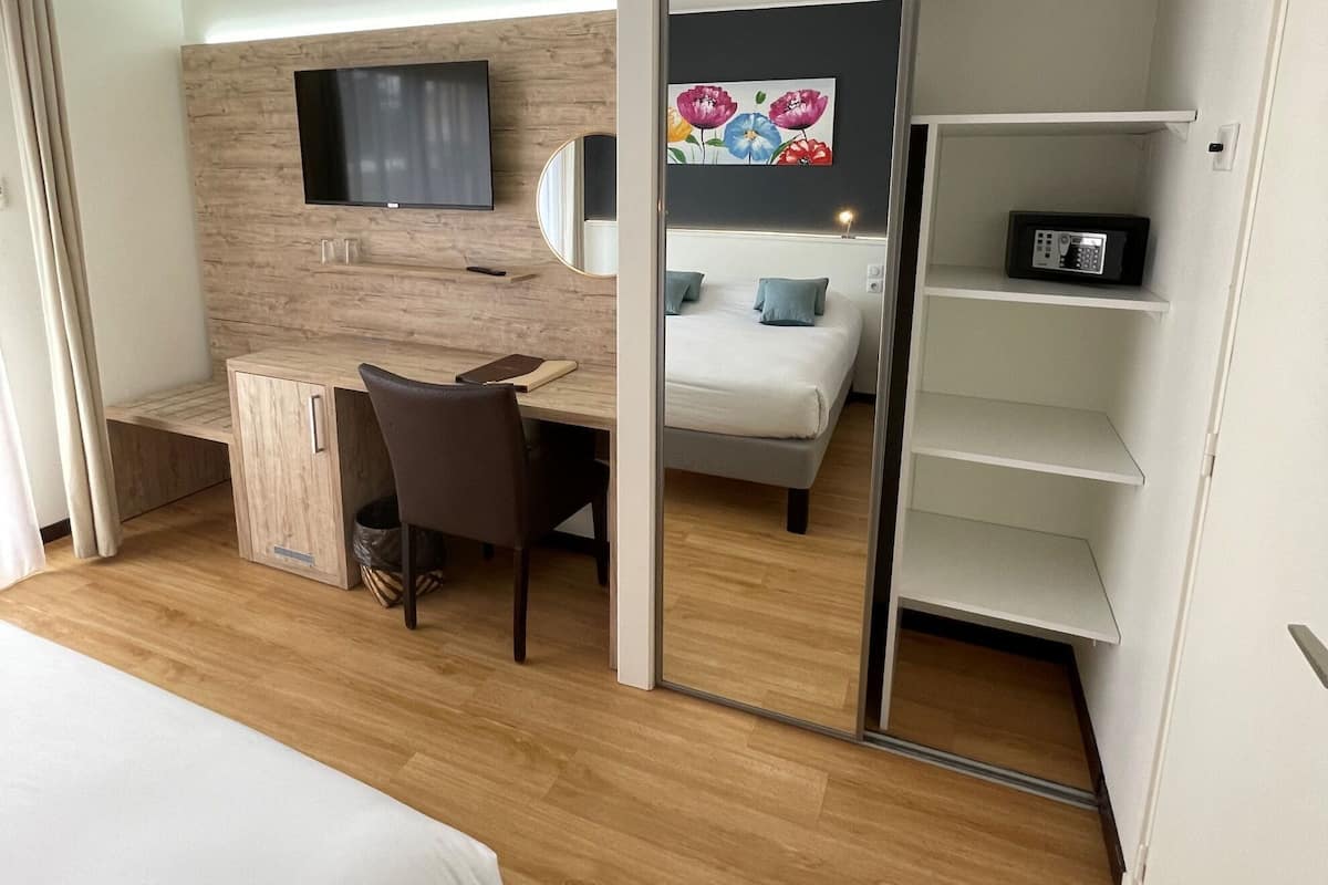 Una camera d'albergo con un letto, una scrivania con una sedia, una televisione, uno specchio, un armadio e un bagno con doccia.
