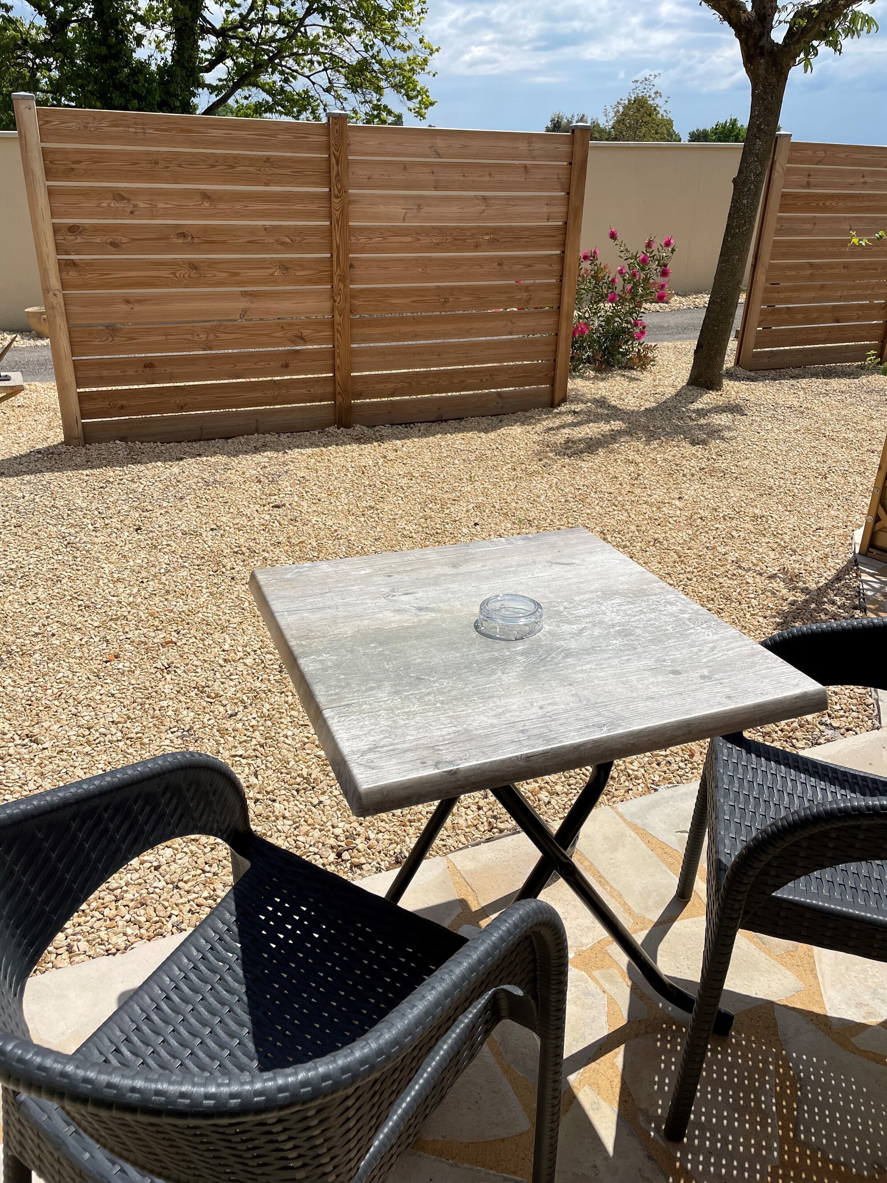 Un patio al aire libre con una mesa cuadrada y dos sillas de mimbre.