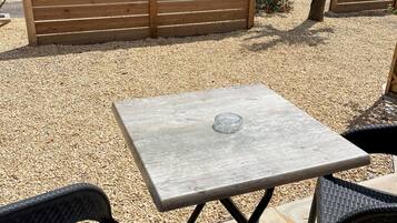 Un patio al aire libre con una mesa cuadrada y dos sillas de mimbre.