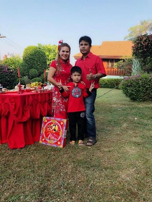 Una familia de pie frente a una mesa con mantel rojo, una caja decorativa y follaje en el fondo.