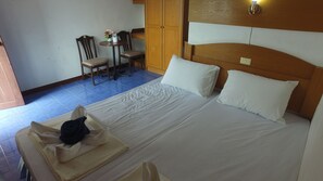 Una habitación de hotel con una cama, dos sillas, una mesita con un florero y un armario.