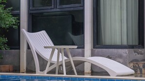 Une piscine avec un fauteuil de relaxation blanc et une fenêtre avec un rideau.