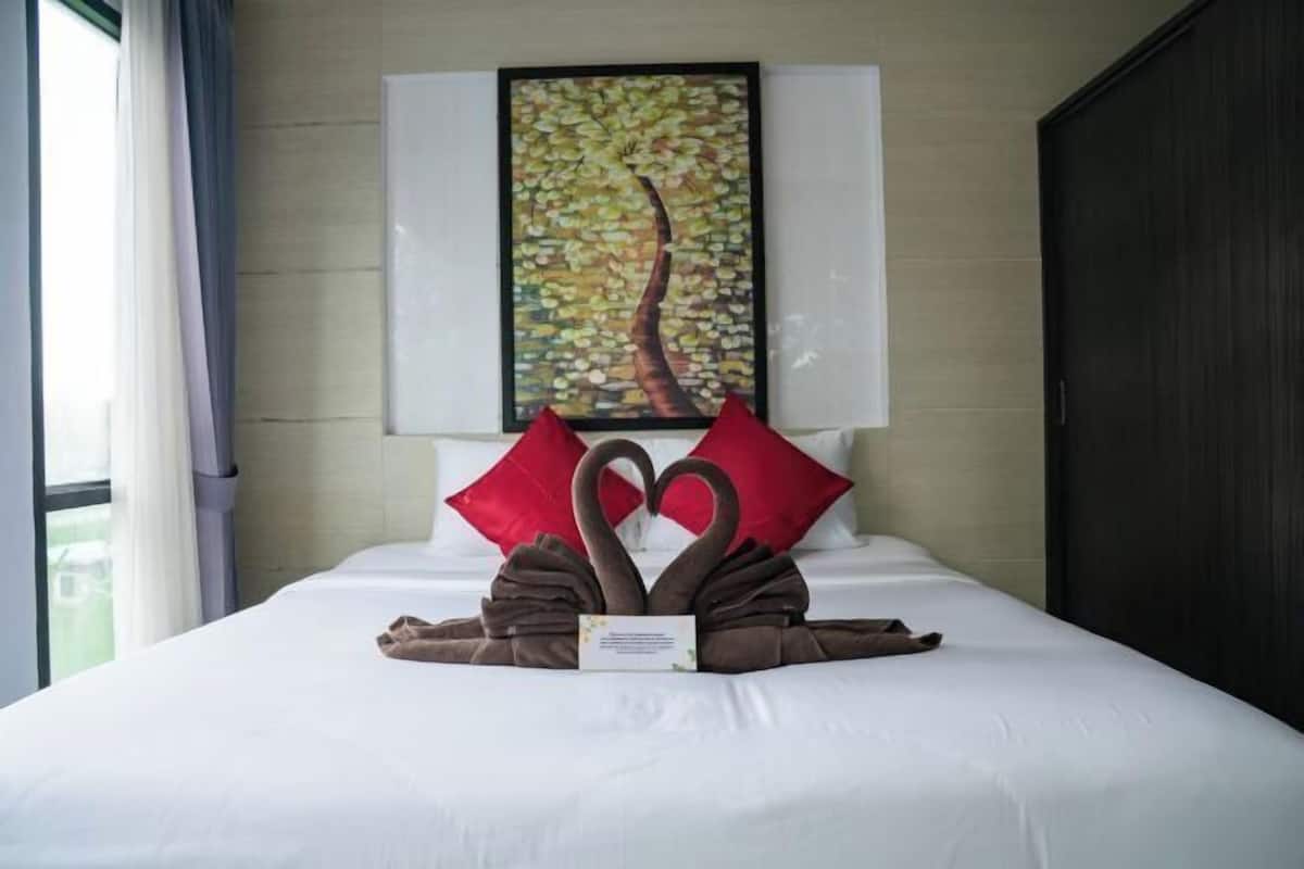 Un lit bien fait, agrémenté d’un coussin en forme de cygne, une œuvre d’art encadrée au mur et une armoire sombre.