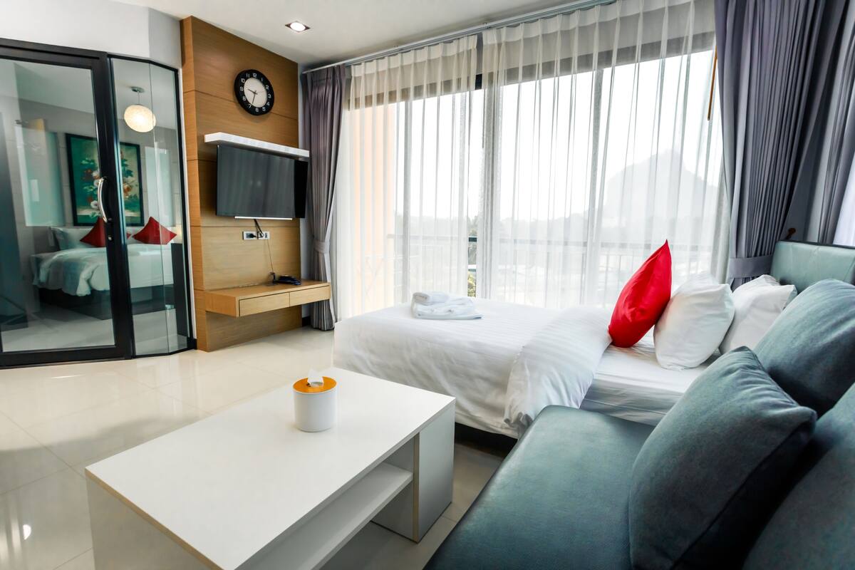 Une chambre d’hôtel moderne équipée d’un lit, d’un canapé, d’une télévision, d’un bureau et d’une fenêtre avec des rideaux.