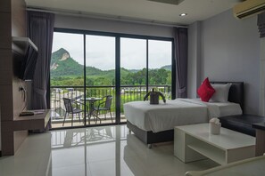 A hotel room with a bed, a desk, a chair, a balcony with a view of greenery and a mountain, and a TV on the wall. - The Lucky Beach Ao Nang (Krabi)