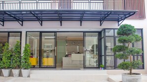 A modern building with a glass entrance, potted plants, and a small tree in a pot. - 168 Studio Hotel Ubon Ratchathani (Ubon Ratchathani)
