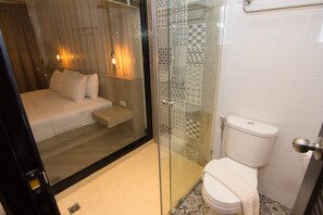 A modern bathroom with a glass shower enclosure, a toilet, and a bed with a white blanket.