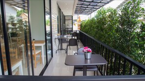 A balcony with a table and chairs, a potted plant, and a view of a building with a traditional roof. - 168 Studio Hotel Ubon Ratchathani (Ubon Ratchathani)