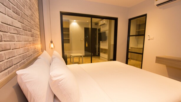 A bedroom with a brick wall, a bed with white bedding, and a sliding glass door leading to a balcony. - 168 Studio Hotel Ubon Ratchathani (Ubon Ratchathani)
