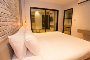 Un dormitorio con pared de ladrillo, cama con ropa de cama blanca y puerta corrediza de vidrio que da a un balcón.