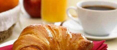 Ein Croissant auf einem Teller mit einer roten Serviette, ein Glas Orangensaft, eine Tasse Kaffee und ein Korb mit einem Apfel und einer Tomate.