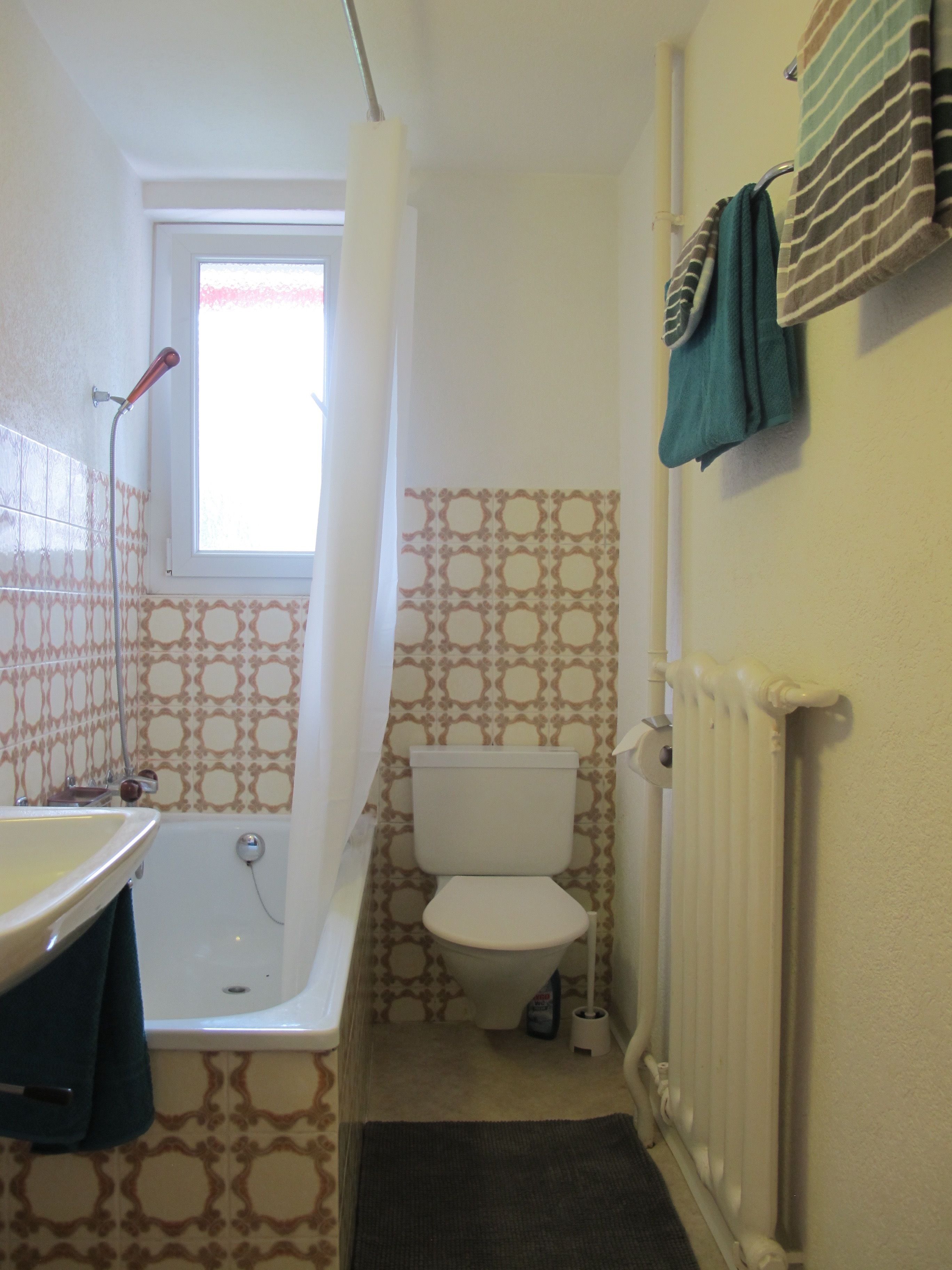 A small bathroom with a bathtub, toilet, and a radiator.