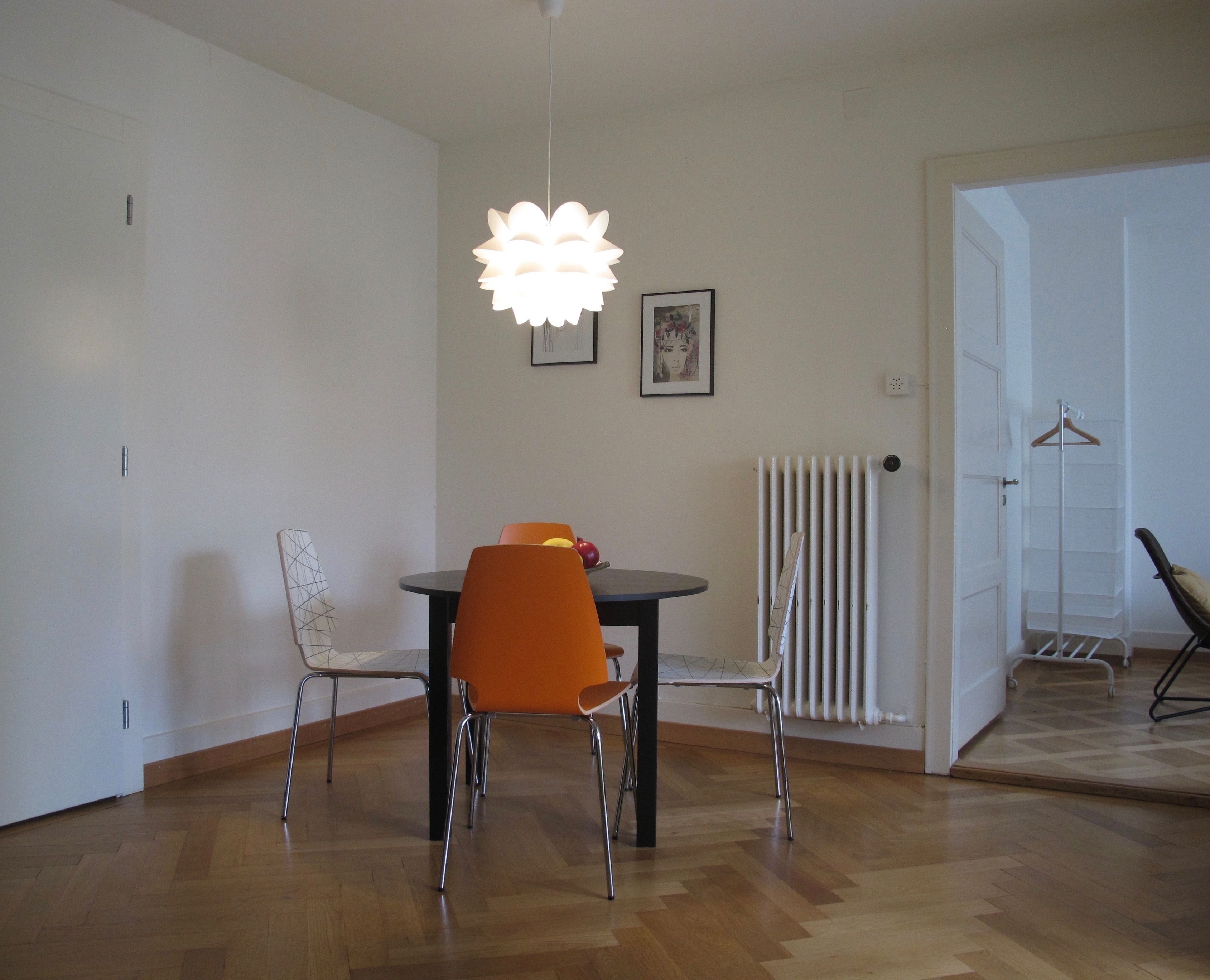 A dining area with a table and chairs, a hanging light fixture, a radiator, and a coat rack.