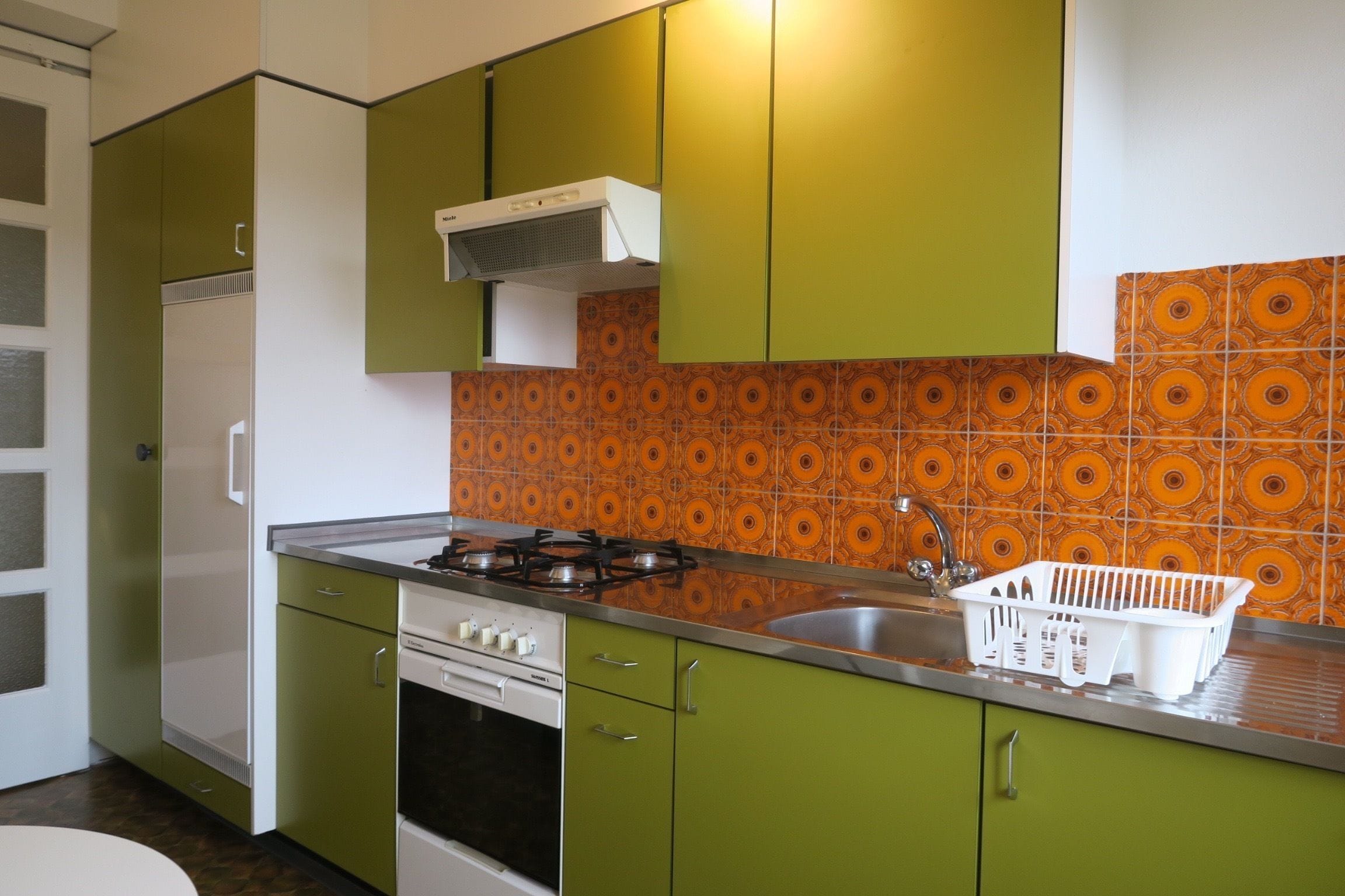 A kitchen with green cabinets, a gas stove, a white oven, and a patterned backsplash.