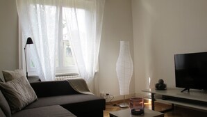 Una sala de estar con sofá, televisión, lámpara y un florero.