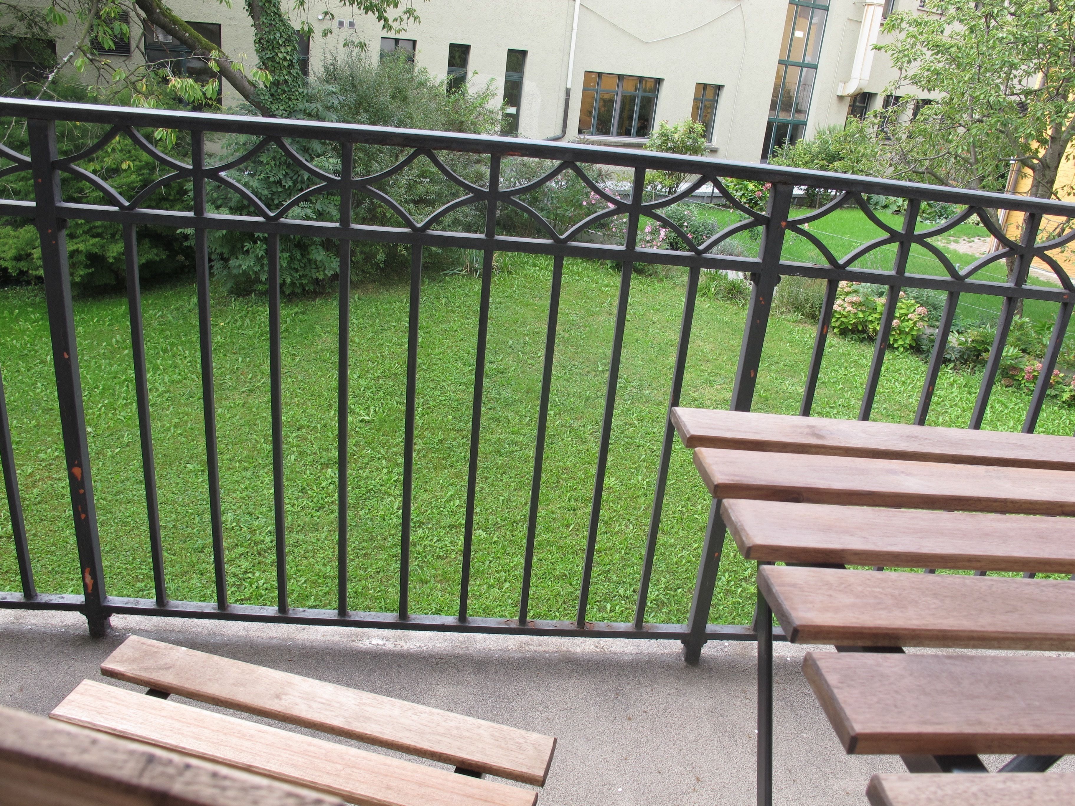 Een balkon met een metalen hekwerk met uitzicht op een gazon en een gebouw op de achtergrond.