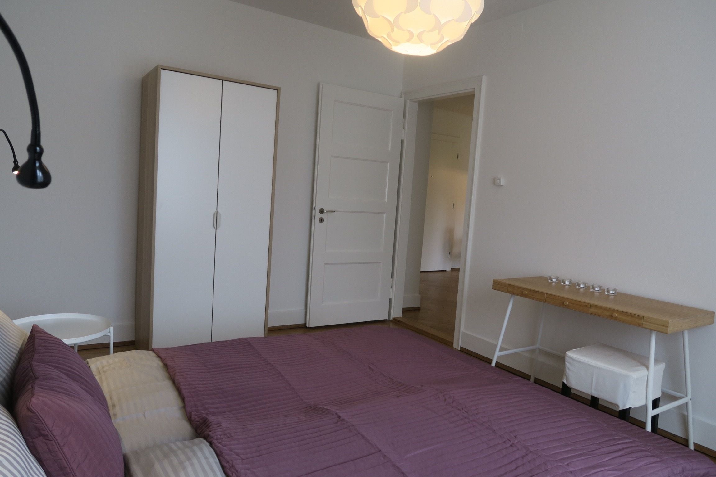 A bedroom with a bed, a desk, a wardrobe, and a hanging lamp.