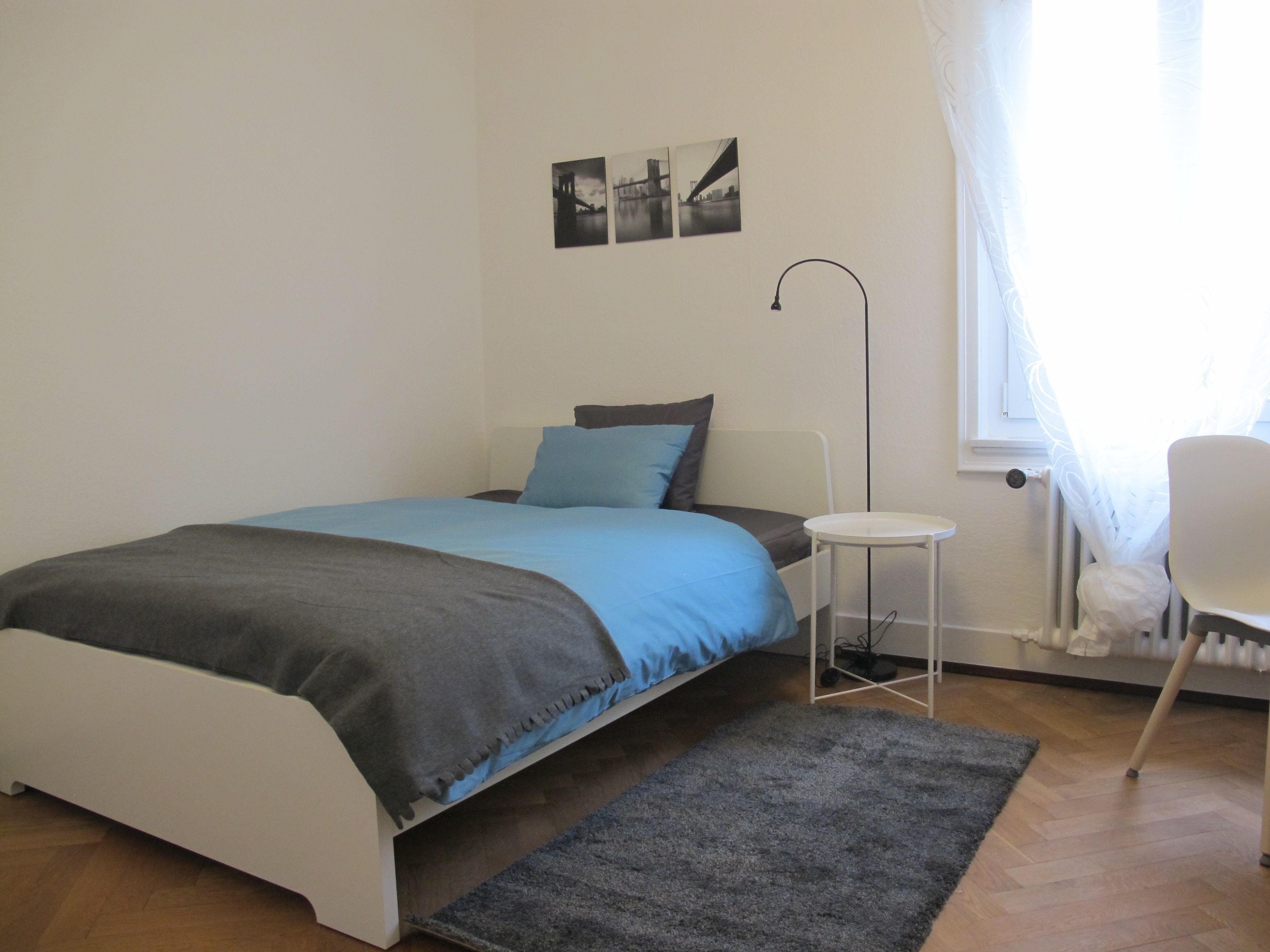 Een slaapkamer met een bed, een klein wit tafeltje, een stoel en een radiator.