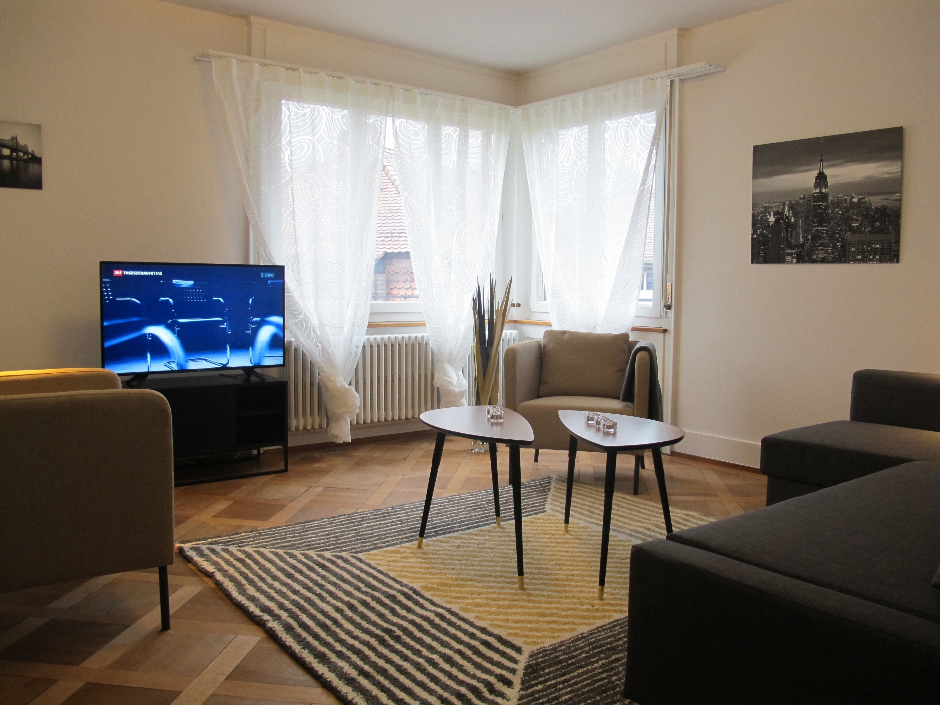Ein Wohnzimmer mit Fernseher, zwei kleinen Tischen, einer Couch und einem Sessel.