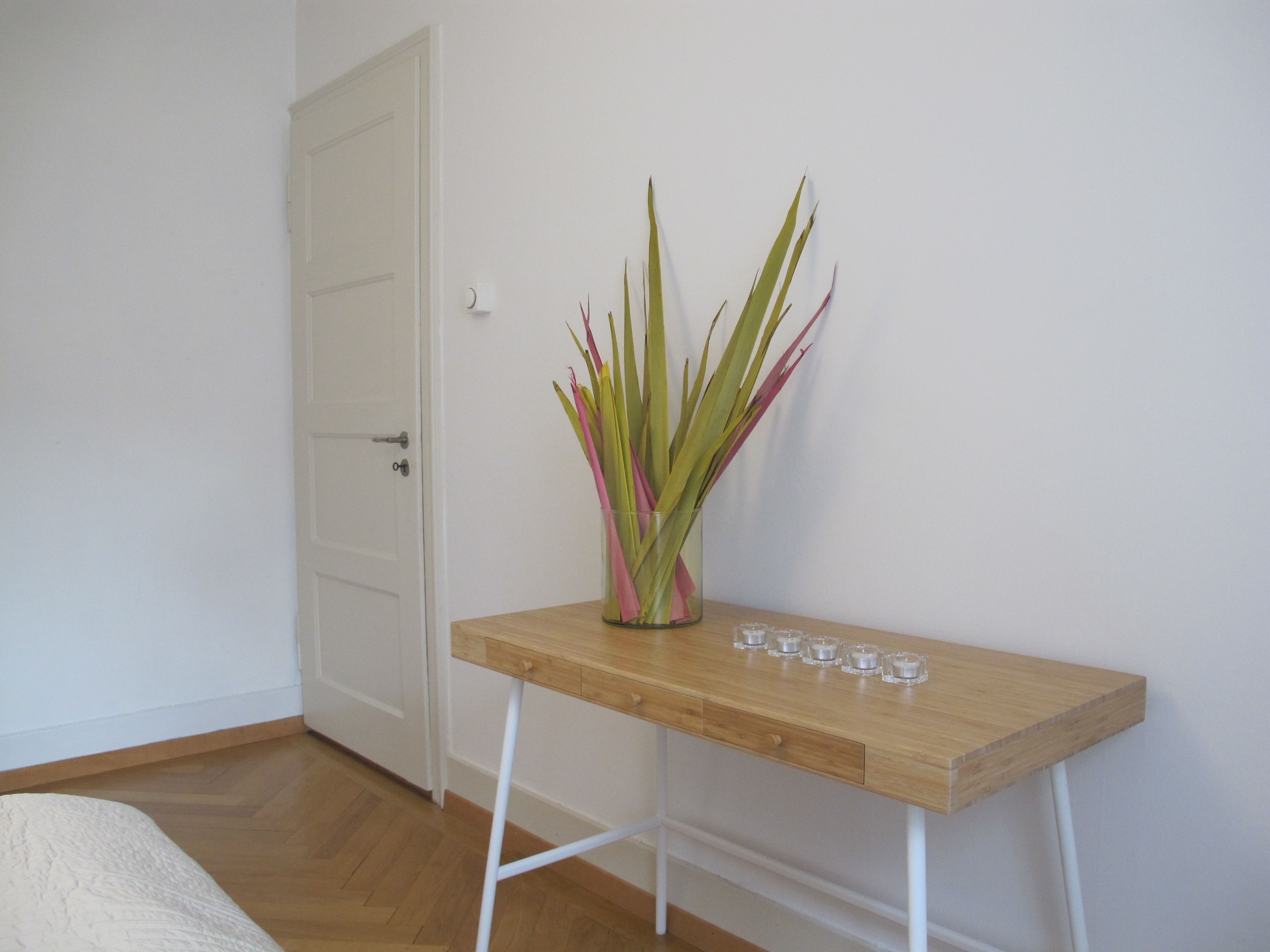 Une pièce avec une table en bois, un vase contenant des feuilles vertes et roses, et une porte blanche.