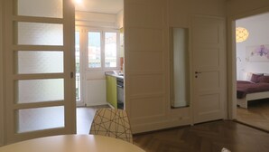 Una habitación con una puerta blanca, una mesa de comedor con una silla y una cama con una colcha morada.