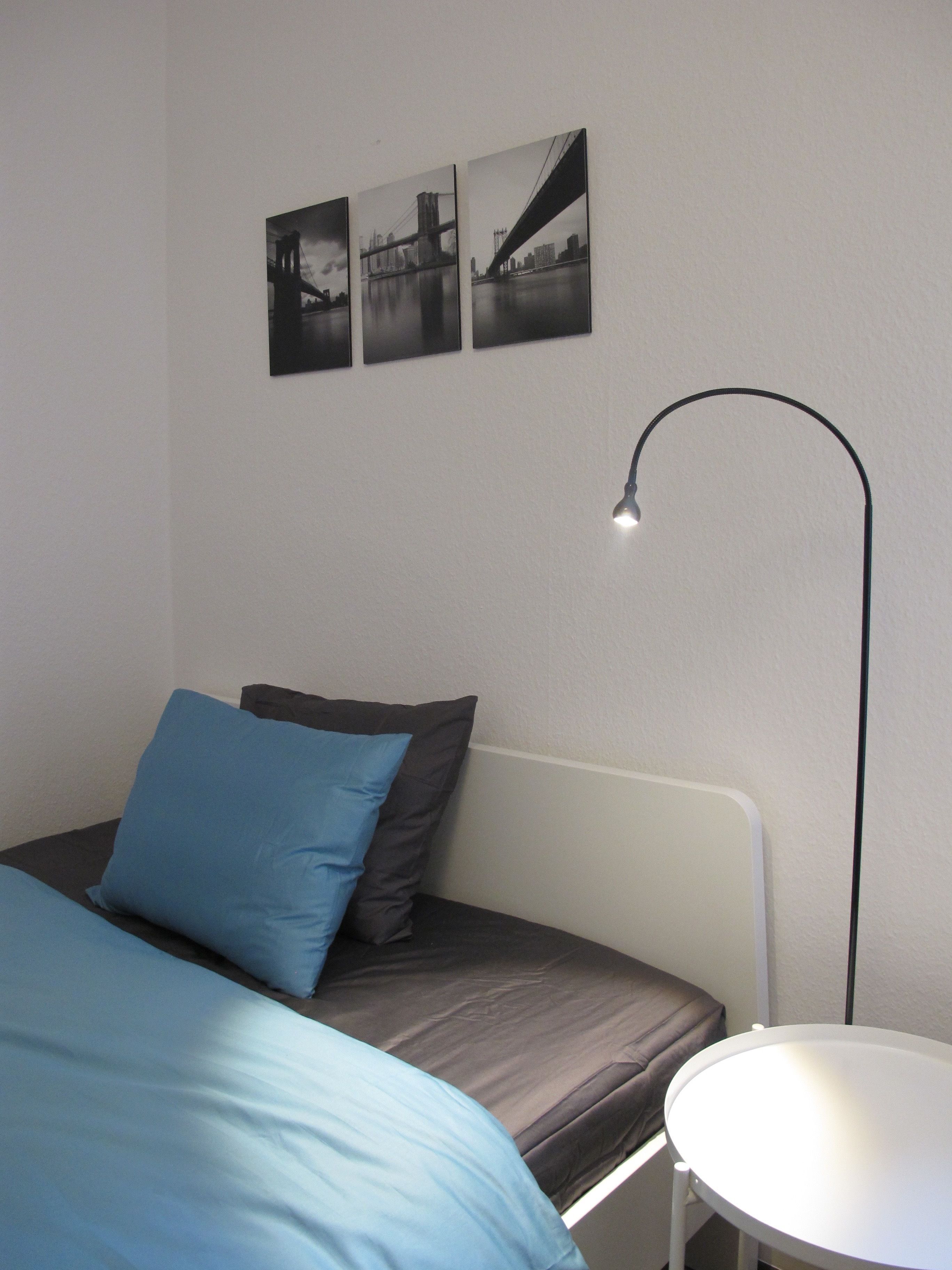 Un dormitorio con cama, almohadas, una mesita de noche y una lámpara de pie.