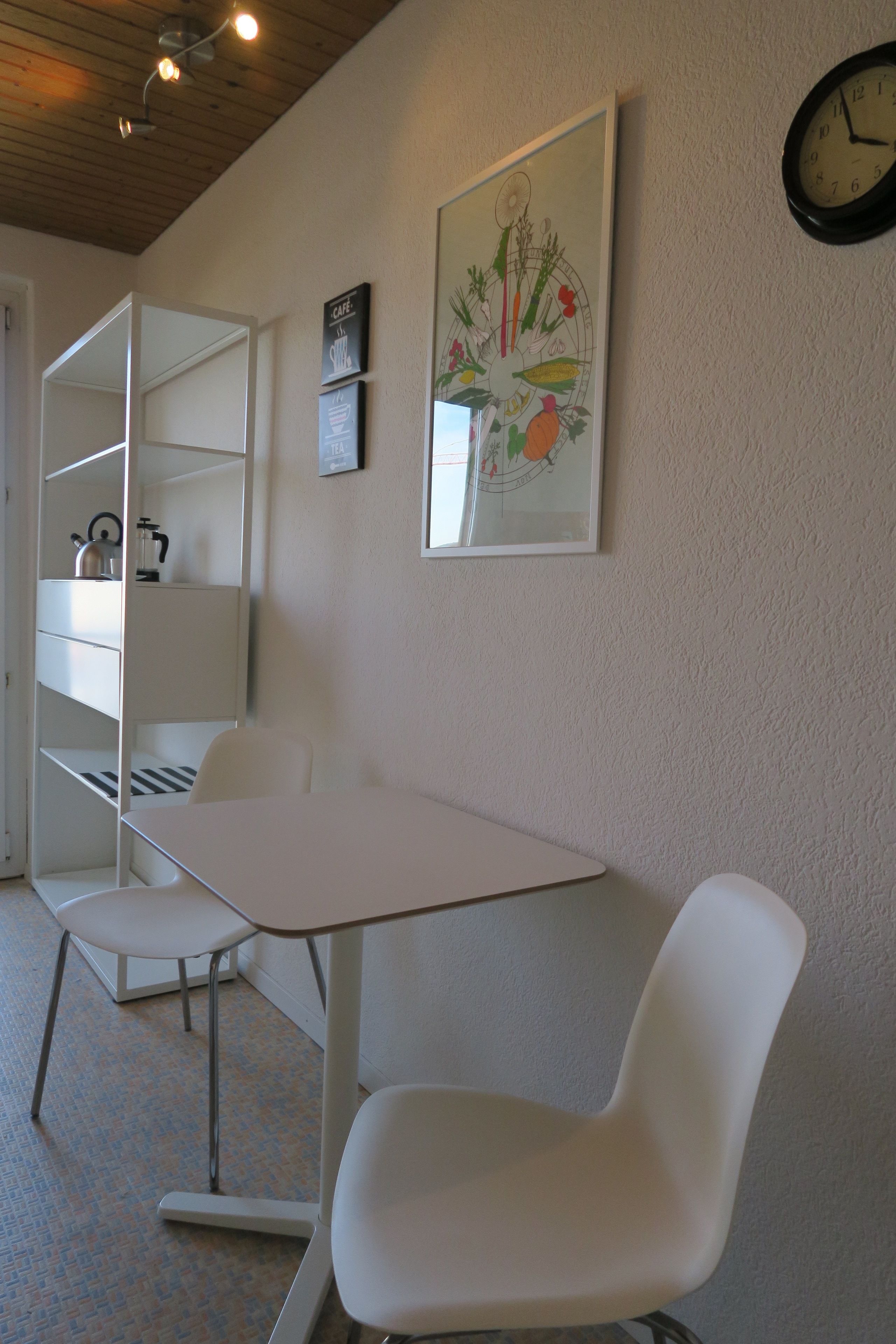 Een kamer met een witte tafel, twee witte stoelen, een klok en een lijst met een afbeelding aan de muur.