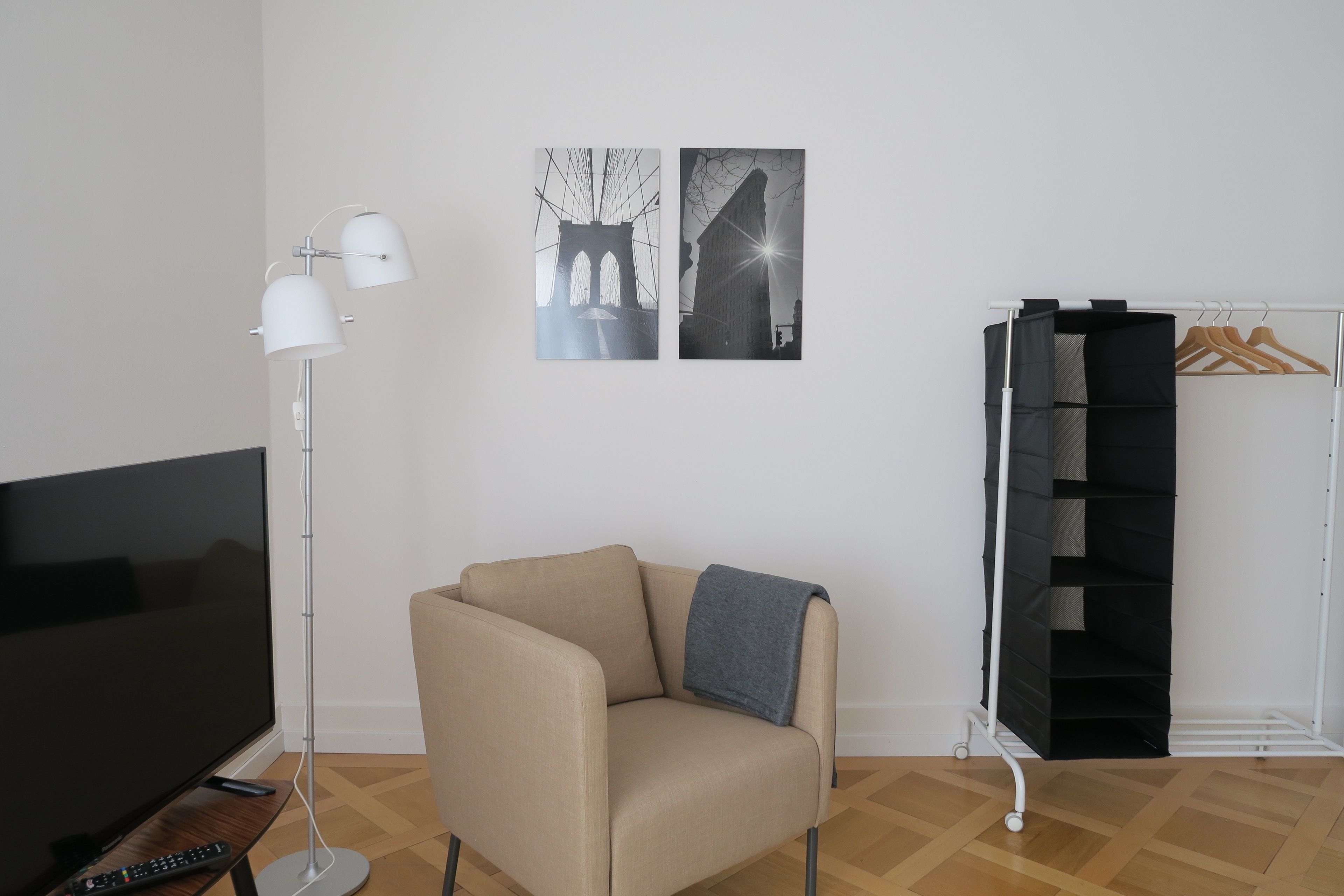 Ein Wohnzimmer mit einer Couch, einer Stehlampe, einem Fernseher und einem Kleiderständer mit Kleiderbügeln.