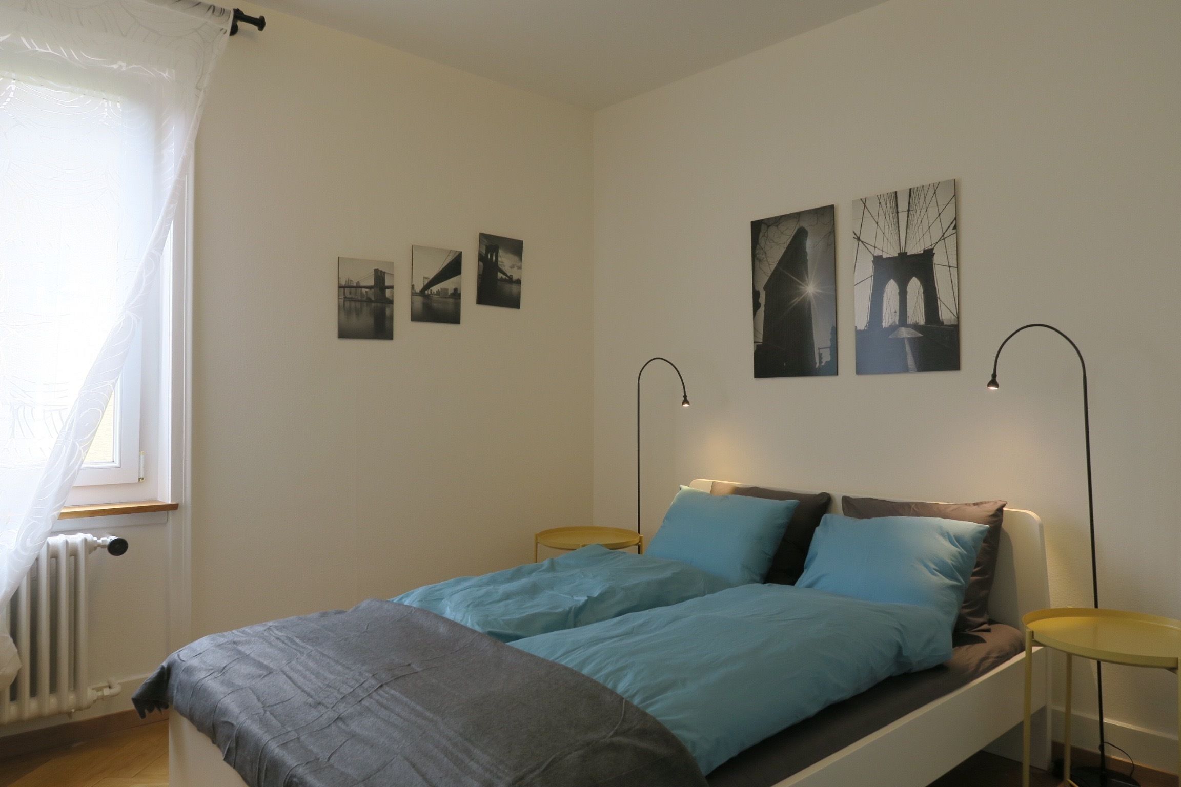 Ein Schlafzimmer mit einem Bett, zwei Nachttischen, einem Heizkörper und drei Bildern an der Wand.